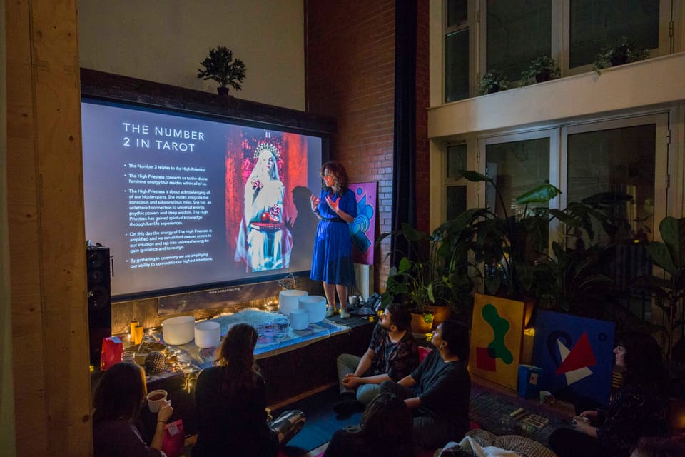 A speaker presenting to a seated audience in front of the projector screen