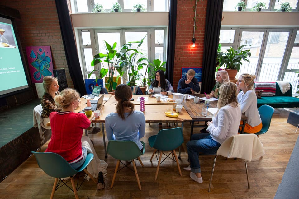 A team working around the long wooden table beside the windows