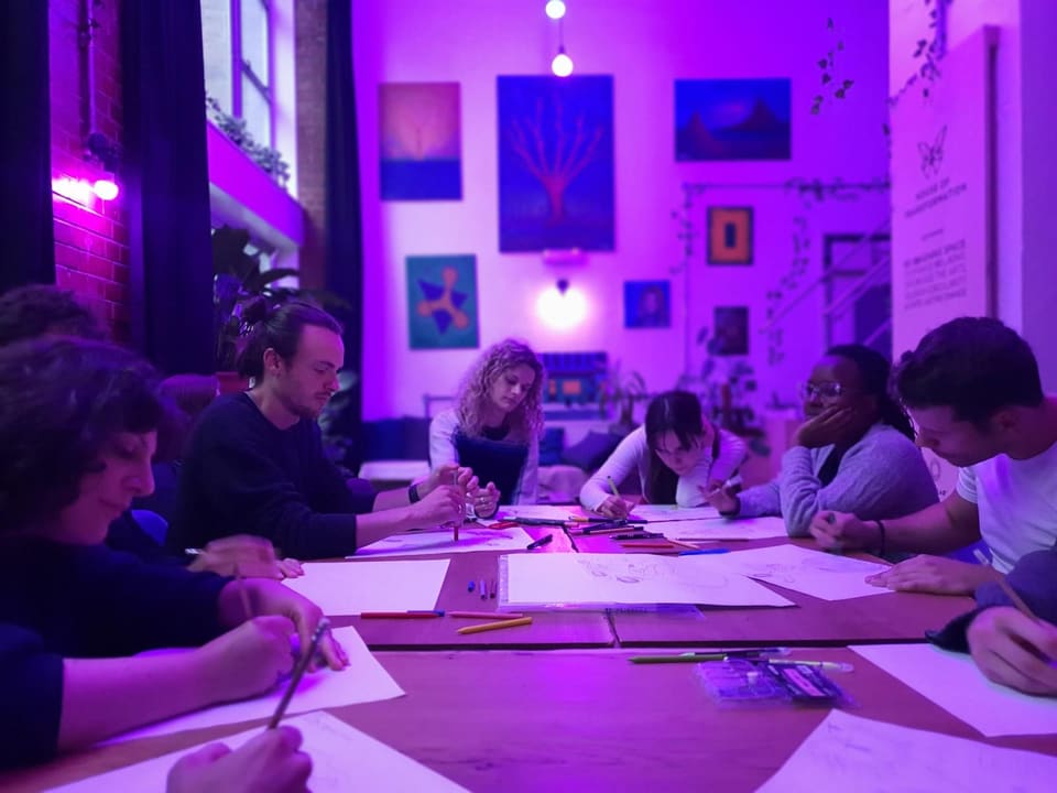 A workshop group working on large sheets of paper under purple lighting
