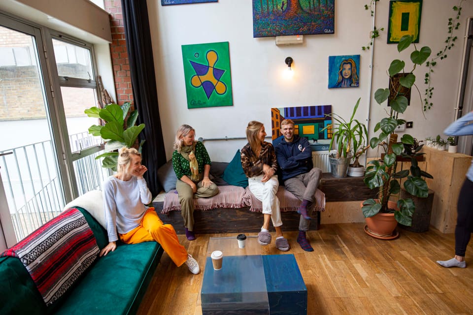 Four people sitting and talking on the low bench beneath the artwork